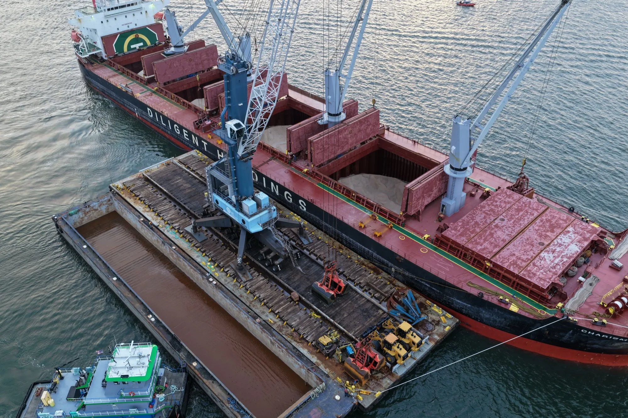 Aerial view of the ship and the crane barge alongside, the grab working an open hold of rock salt, a tug and an empty barge standing by