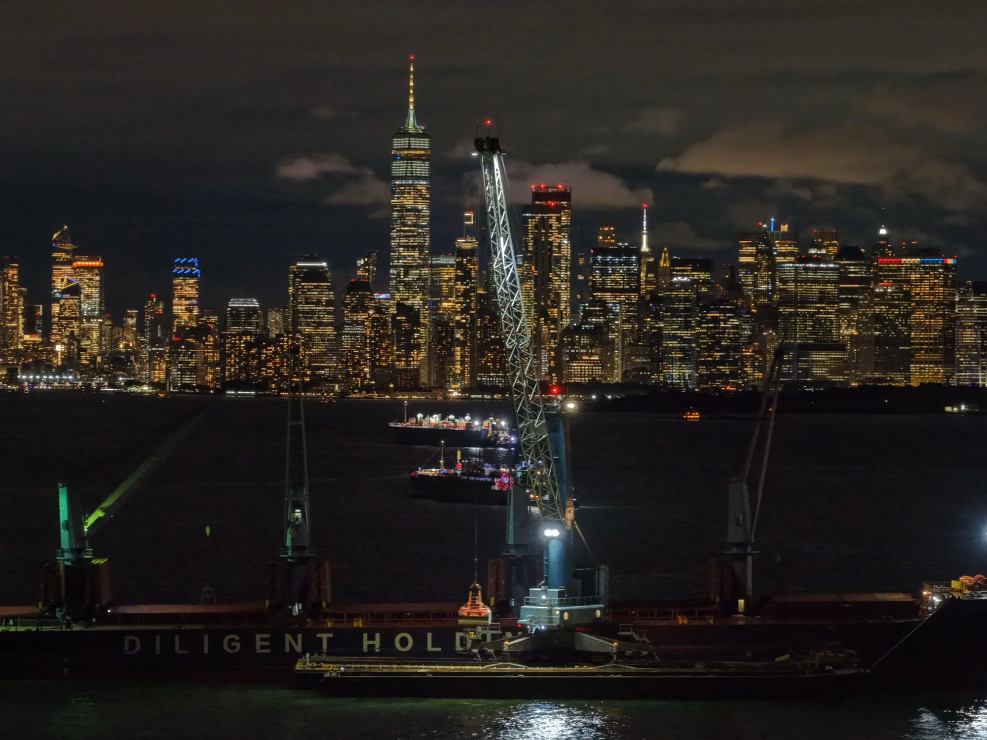 The crane working the ship at night, the lit Lower Manhattan skyline behind it