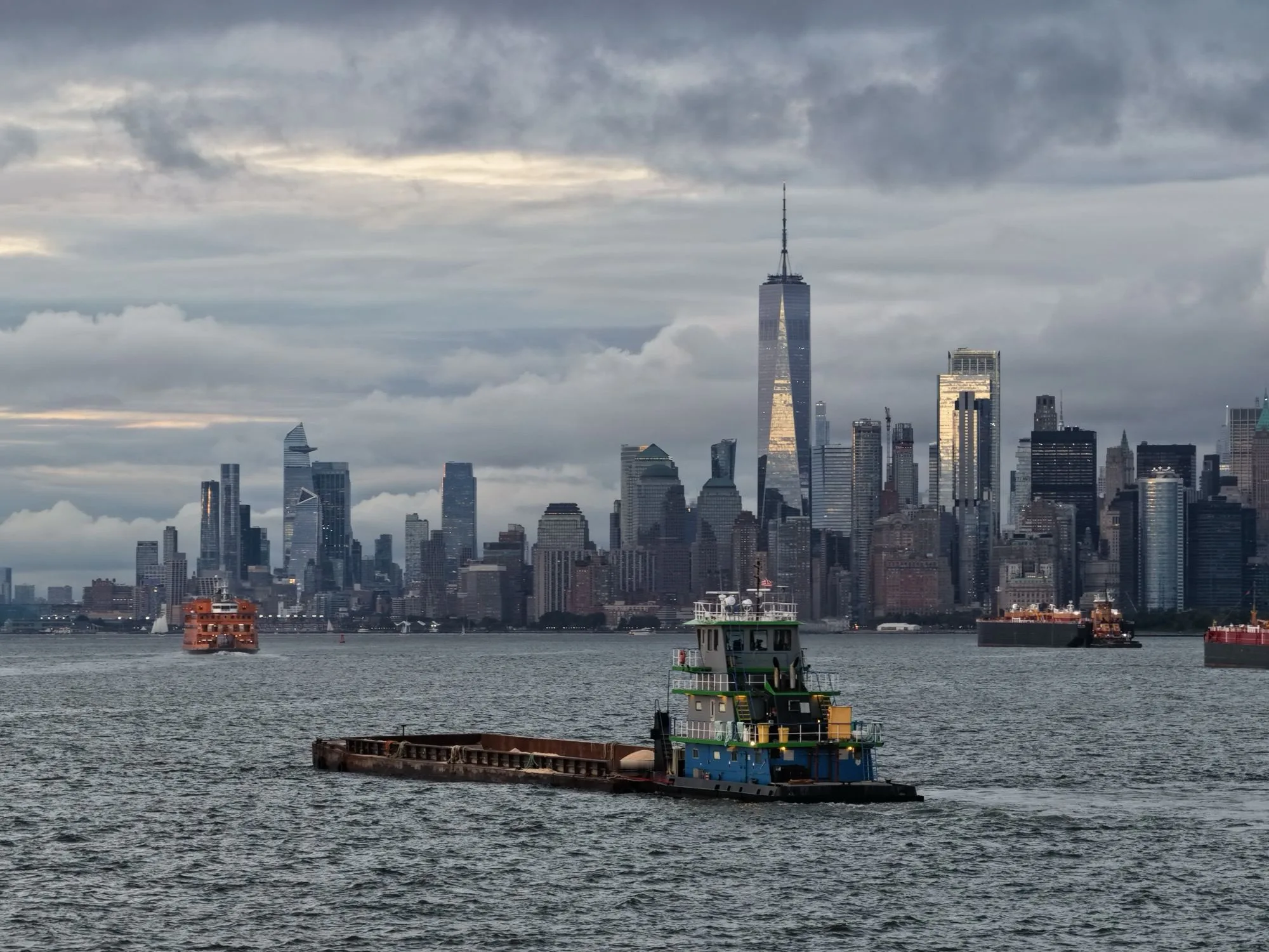 A tug pushing a barge of rock salt across New York Harbor, with the Lower Manhattan skyline behind