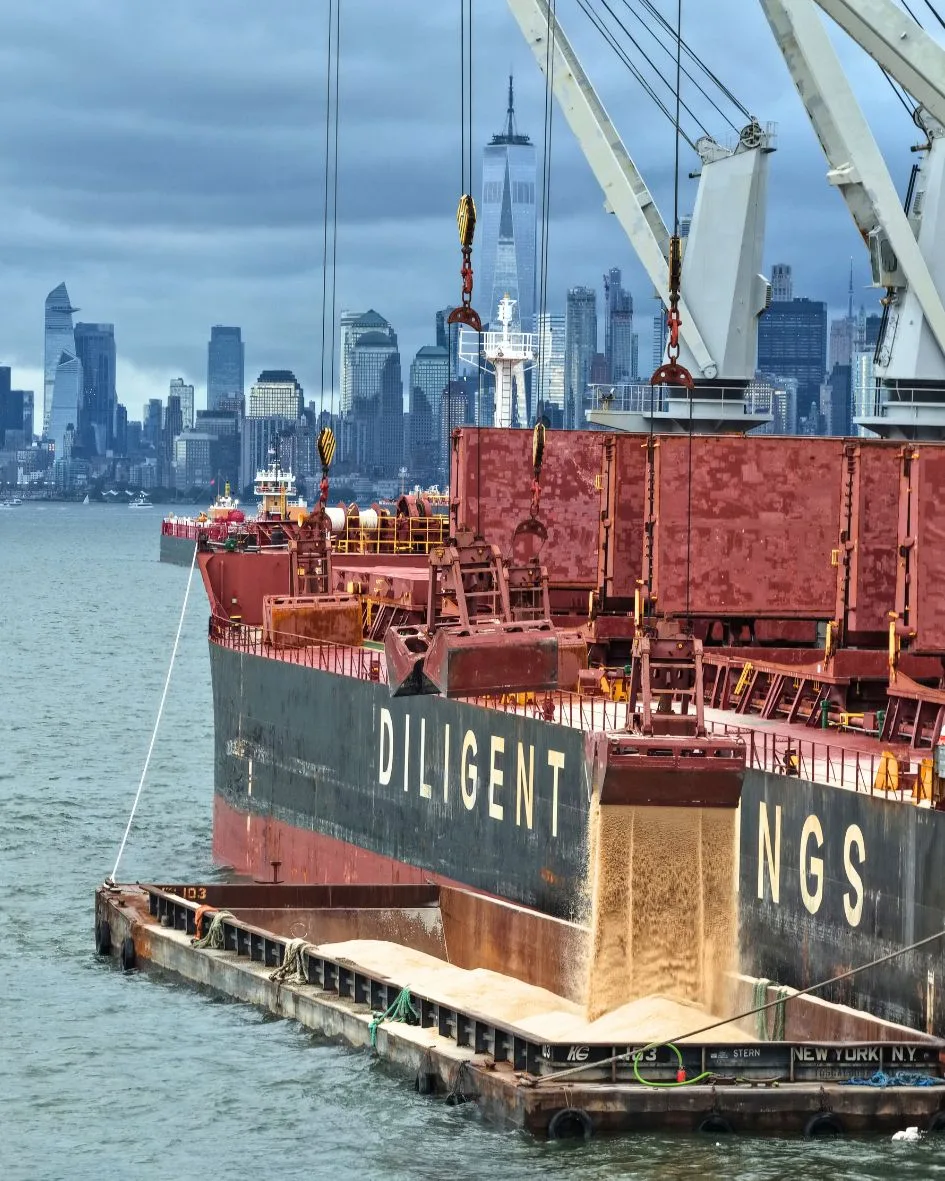Salt pouring from the grab into a barge alongside the ship's hull, the Manhattan skyline behind